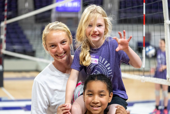 2 Campers and a coach smiling next to volleyball net